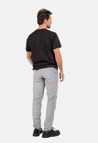 Men's outfit featuring a black cotton T-shirt and light gray pants. The pants have a smooth texture and notable side pockets. Black footwear.