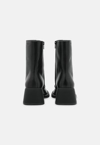 Svarta läderankelboots med hög skafthöjd, kantig blockklack och dragkedjestängning på sidan; slät yta med subtilt varumärkesdetalj.