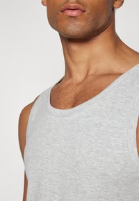 Graues Baumwoll-Top mit weitem Ausschnitt und ärmellosem Design, das eine glatte Textur und ein dezentes Melange-Muster aufweist.