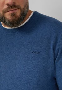 Blauer Pullover aus weichem Stoff mit rundem Ausschnitt. Auf der Brust befindet sich ein kleines schwarzes "s.Oliver"-Logo. Glatte Textur, lässiges Design.