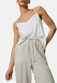 Weißes Leinen-Camisole mit dünnen Trägern, kombiniert mit beigen gestreiften Hosen mit Kordelzug aus leichtem Stoff, die einen lockeren Sitz bieten.