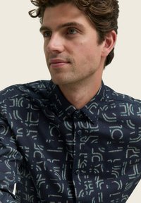 Navy gekleed shirt met elkaar kruisende lichtblauwe lijnen, knopen ontwerp, korte kraag en textuurstof. Close-up weergave.