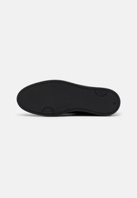 Suela de zapato de goma negra con una superficie texturizada, que presenta una forma redondeada y un borde suave. Incluye un detalle en relieve que dice "Hecho en Portugal".