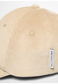 Beige corduroy pet met een gestructureerd oppervlak, afgeronde vorm en gestikte accenten, met een label waarop "Marc O’Polo DENIM" staat.