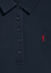 Mörkblå pikétröja i strukturerat tyg, med en treknapps placket och en röd broderad logotyp av en golfare.