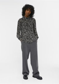 Zwart-wit gestreepte blouse met lange mouwen, gecombineerd met losse grijze broeken en zwarte chunky schoenen. Gladde stofstructuur.