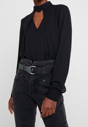 Czarna bluzka z wysokim kołnierzem i wycięciem w kształcie litery V, zestawiona z czarnymi jeansami z wysokim stanem oraz matowym paskiem z metalową klamrą.