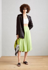 Svart blazer, hvit crop topp, grønn kne-lengde skjørt, svarte sandaler og mønstrete håndveske. Teksturert stoff, moderne silhuett.