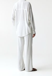 Camicia bianca dalla vestibilità ampia abbinata a pantaloni bianchi a gamba larga, realizzati in tessuto leggero, con polsino con bottoni e orlo arrotondato.