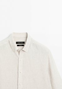 Light beige linen button-down shirt with a collar and white buttons, displayed against a plain white background.