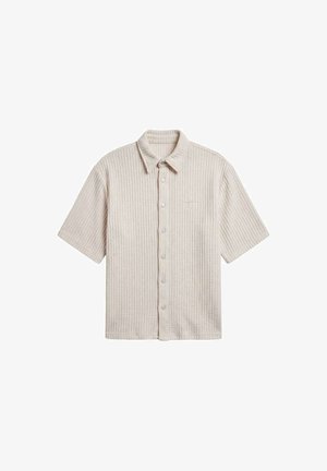 Chemise à manches courtes en tricot gaufré beige avec col et boutons pression à l'avant, présentée à plat sur un fond blanc.