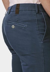 Dunkelblaue Hose aus strukturierter Stoff, mit einer hinteren Tasche mit Knopfverschluss und einem Lederpatch in der Nähe des Bundes.