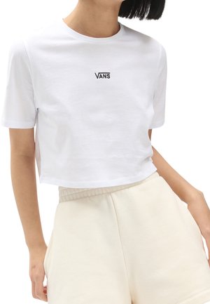 Personne portant un t-shirt blanc court Vans et un short taille haute crème, posant avec une main dans la poche sur fond blanc.