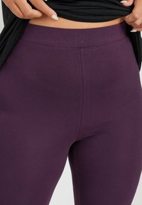 Mallas moradas con una textura suave, cintura alta y diseño sin costuras, sin patrones ni acentos visibles. La tela es elástica y ajustada.