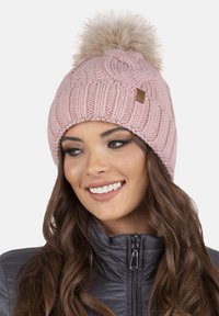 Berretto rosa lavorato a maglia con un motivo texturizzato, rifinito da un pompon soffice. Presenta un piccolo etichetta marrone attaccata al bordo.