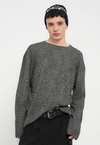 Γκρι μακρυμάνικο πουκάμισο με διακριτικό μοτίβο λεοπάρδαλης, σε άνετη εφαρμογή και στρογγυλή λαιμόκοψη, συνδυασμένο με μαύρο παντελόνι με ζώνη.