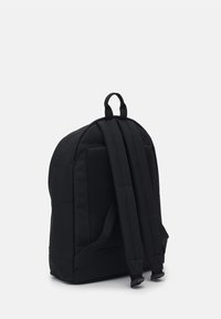 Mochila de tela negra con respaldo acolchado, correas ajustables y textura suave. Cuenta con un asa superior y acentos de malla para transpirabilidad.