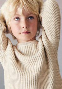 Beige gestrickter Pullover mit geripptem Muster, Rundhalsausschnitt und langen Ärmeln; der weiche Stoff fällt leicht über die Schultern.