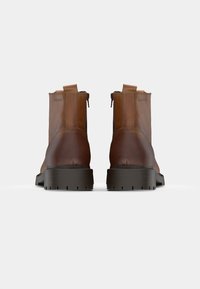 Botas de cuero marrón hasta el tobillo con un acabado suave, paneles laterales elásticos y una suela de goma negra robusta. Cierre con cremallera en la parte trasera.