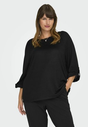 Zwarte losse top met een ronde halslijn en driekwartopgerolde mouwen, gemaakt van zachte stof, gecombineerd met zwarte broek.