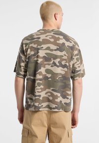 Beige camouflage t-shirt met korte mouwen, versierd met groene en bruine patronen. Gemaakt van lichtgewicht stof, met een ronde hals en een relaxte pasvorm.