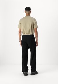 Beige katoenen t-shirt en zwarte broek met een relaxte pasvorm. De broek heeft achterzakken en een platte tailleband. Zwart schoeisel zichtbaar.