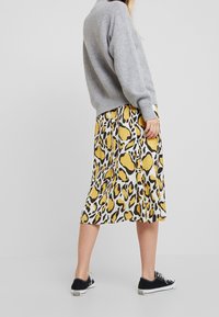 Šedý pletený svetr a plisovaná midi sukně s designem žlutočerného zvířecího vzoru, v kombinaci s černými plátěnými teniskami.