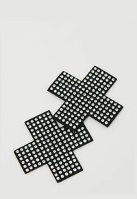 Dvě černé samolepicí náplasti ve tvaru kříže pokryté rovnoměrně rozmístěnými malými stříbrnými kamínky na světlém pozadí.