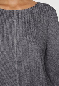 Graues geripptes Strickoberteil mit weitem Rundhalsausschnitt, das eine subtile Naht in der Mitte und eine glatte Textur aufweist.