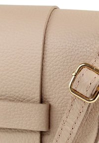 Beige leren handtas met een gestructureerde afwerking. Voorzien van een gesp met gouden hardware en een riem met gestikte accenten. Compact en rechthoekig van vorm.
