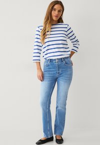 Blauwe en witte gestreepte longsleeve top met een ronde hals, gecombineerd met lichtblauwe rechte jeans en zwarte platte schoenen.