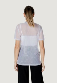 Camiseta blanca transparente de manga corta, con una textura estampada y un panel liso en la parte posterior. Incluye un cuello redondo y un corte relajado.