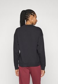 Sudadera negra con mangas largas, cuello redondo y dobladillo acanalado. Llevada con pantalones burdeos, mostrando un ajuste relajado y textura de la tela.