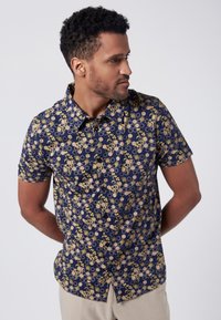 Camicia a maniche corte con bottoni di colore blu navy, dotata di un motivo geometrico a nido d'ape e accenti floreali in giallo e beige. Tessuto dal tocco morbido.