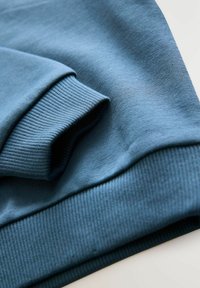 Blå sweatshirt detaljer med ribbet mansjet, glat tekstur og subtil strækstof. Designet er enkelt uden synlige mønstre.