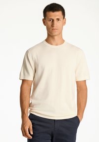 Krämfärgad kortärmad t-shirt med rund halsringning, tillverkad av mjukt tyg, med en avslappnad passform och subtil textur.