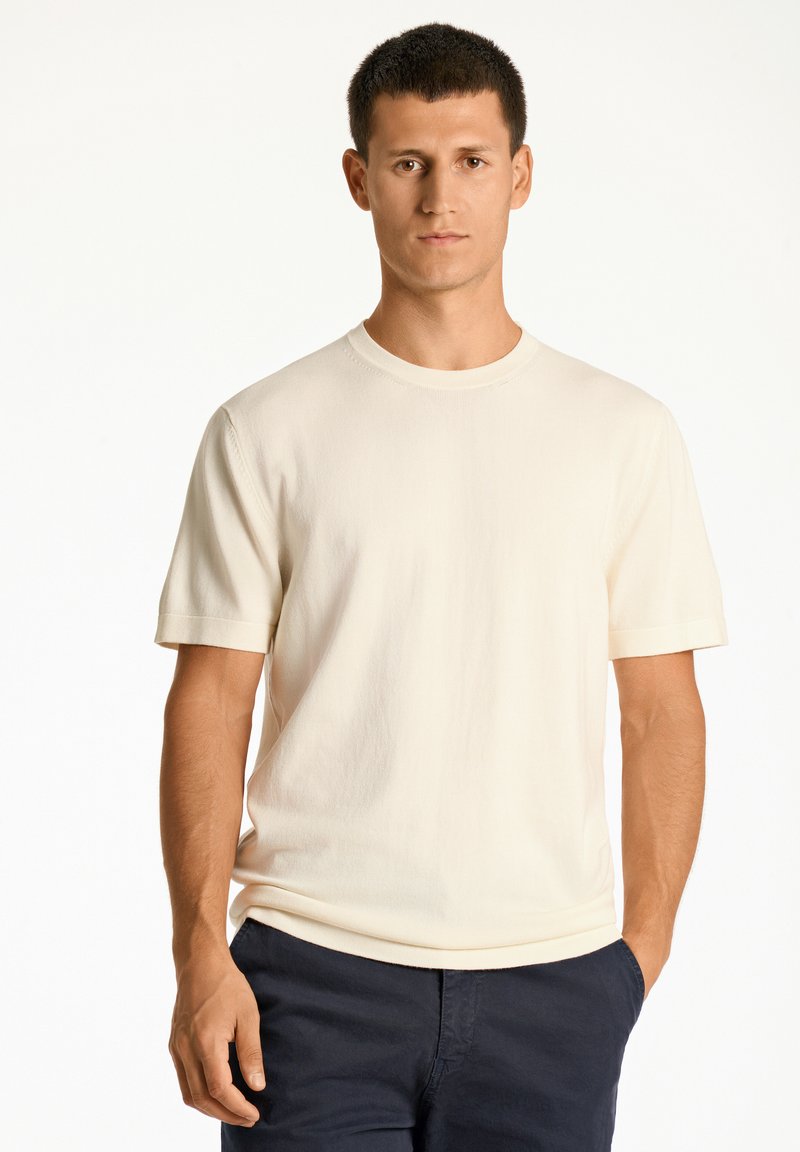 Krämfärgad kortärmad t-shirt med rund halsringning, tillverkad av mjukt tyg, med en avslappnad passform och subtil textur.