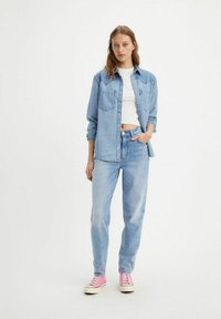Lichtblauw denim shirt met knopen aan de voorkant en twee borstasjes, gecombineerd met lichtblauwe jeans en roze sneakers. Eenvoudig, casual ontwerp.