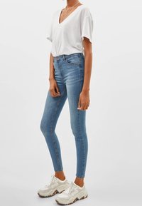 Ljusblå skinny jeans med hög midja, tillverkade av denim. Tillsammans med en lös vit V-hals t-shirt och vita sneakers med bruna detaljer.
