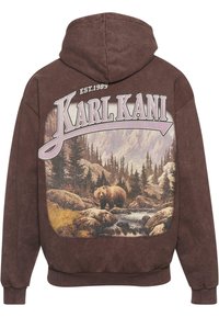 Barna kapucnis pulóver puha anyagból, amelyen egy folyó mellett és erdőben álló medve grafikája látható, valamint a "KARL KANI" és az "EST.1989" felirat.