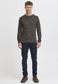 Mørkebrun teksturert genser med lange ermer og rund hals, parret med marineblå bukser og brune mønstrede sko. Enkel og tettsittende design.