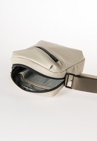 Borsa a tracolla beige con un esterno liscio e resistente all'acqua, chiusura con zip e una tracolla regolabile. L'interno presenta una fodera elegante.