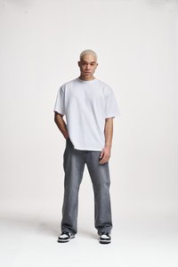 Hvit oversized t-skjorte laget av bomull, kombinert med løse grå jeans og svarte og hvite joggesko, med et enkelt design og en avslappet passform.