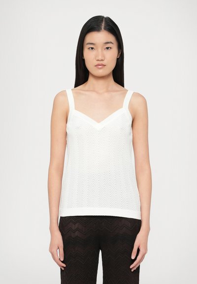 Débardeur blanc avec un motif en chevrons, doté de larges bretelles et d'un décolleté en V. Le tissu semble texturé et léger.