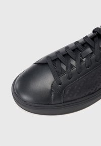 Baskets noires en cuir lisse avec panneau latéral texturé. Bout rond avec système de laçage et design minimaliste.