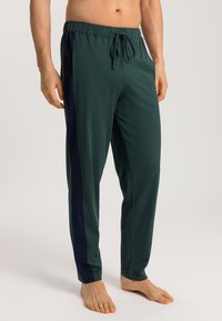 Groene sportbroek met een elastische tailleband en trekkoord, zijzakken en contrasterende navy zijstrepen. Zachte textuur en losse pasvorm.
