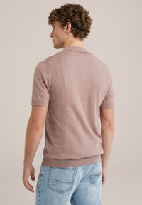 Tricou polo cu mânecă scurtă și guler rotund, dintr-un material roz deschis, având manșete și tiv ribbate, asociat cu blugi din denim albastru deschis.