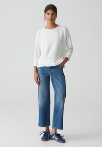 Witte geribde pullover met een ronde hals, gecombineerd met medium blauwe wijde jeans en marineblauwe sneakers met witte strepen.