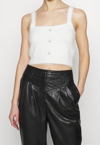 Top bianco a pelo corto con scollatura quadrata, caratterizzato da tre bottoni in perla sul davanti. Abbinato a pantaloni in pelle nera a vita alta.