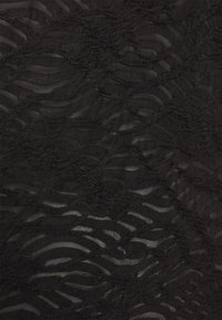 Tissu noir transparent avec des motifs texturés ondulés irréguliers créant un design abstrait en couches.